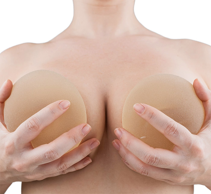 Female breast implant exchange model poses holding a breast implant in each hand in front of breasts at Viradia Plastic Surgery in Tampa, Florida