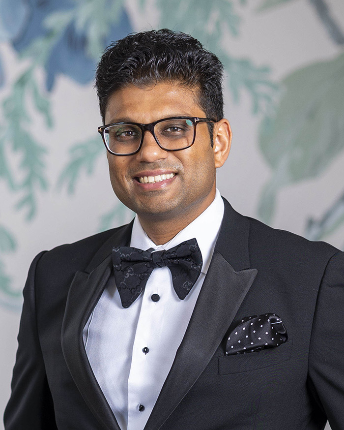 Dr. Viradia smiles in a tuxedo with a floral background.